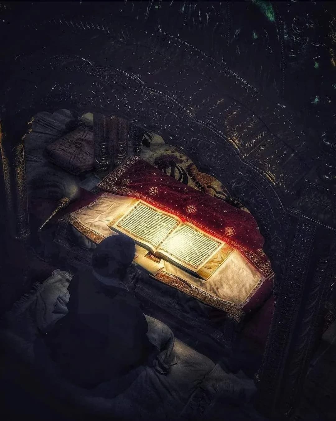 Sri Guru Granth Sahib Ji open and lit in the dark, a Sikh sitting in prayer before it